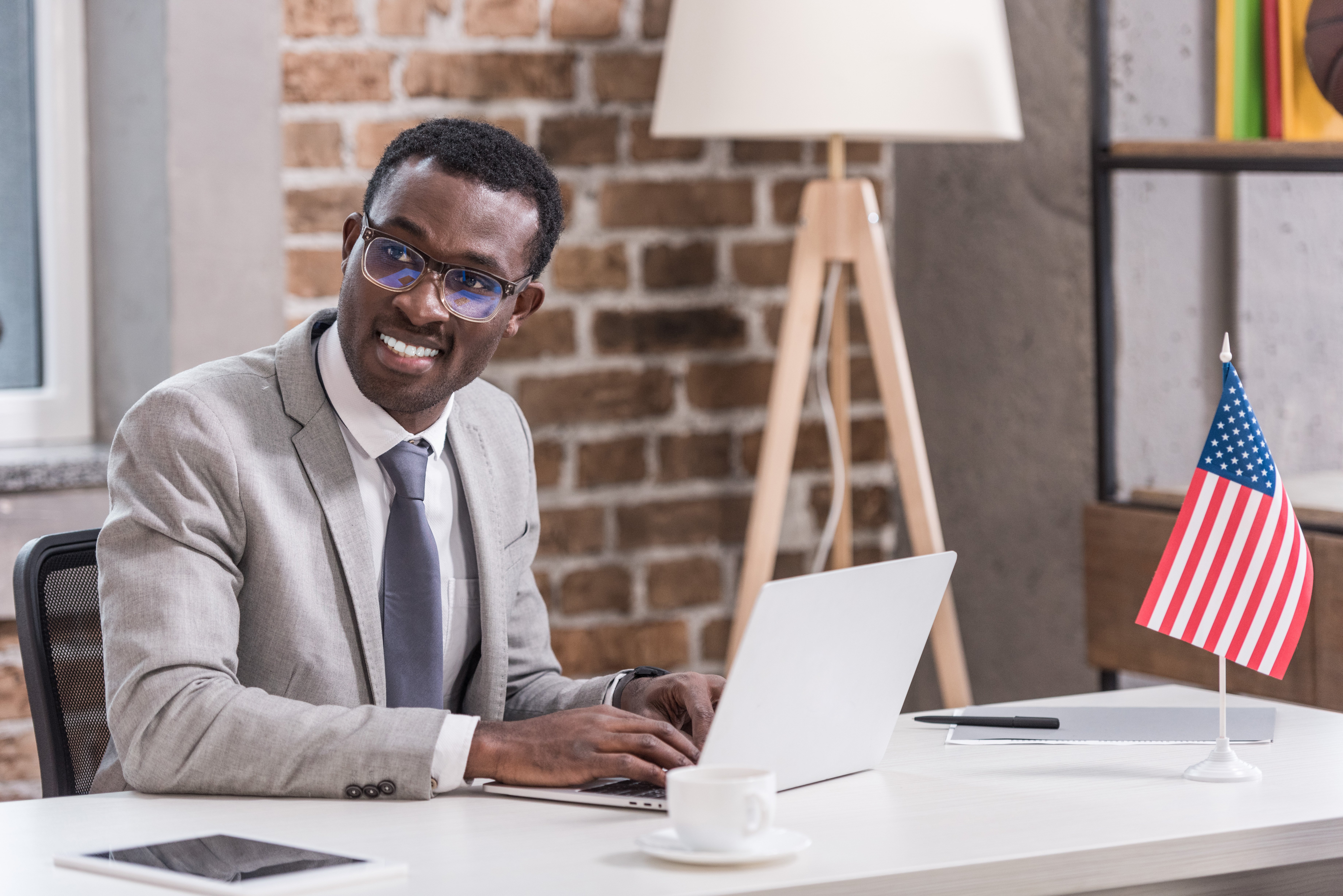 Procurement manager sits at desk with laptop computer, small U.S. flag on desk, reviewing domestic sourcing with a GPO