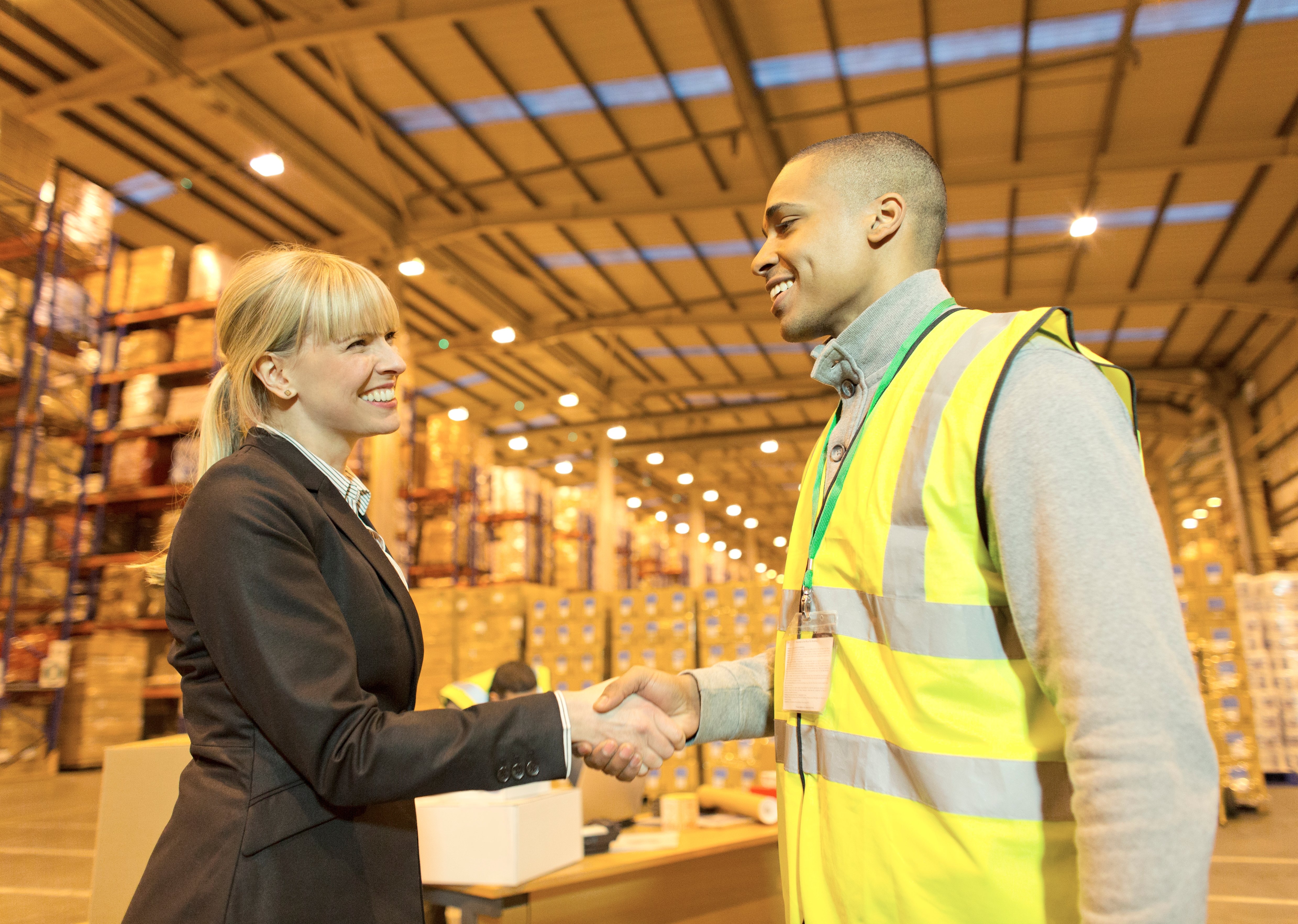 Smiling procurement specialist shakes hands with her supplier’s warehouse manager.

