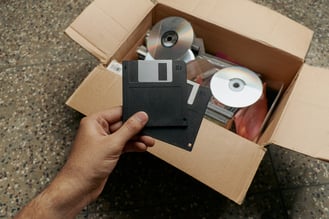 Man places outdated office equipment, including CDs and floppy disks, into a storage box.