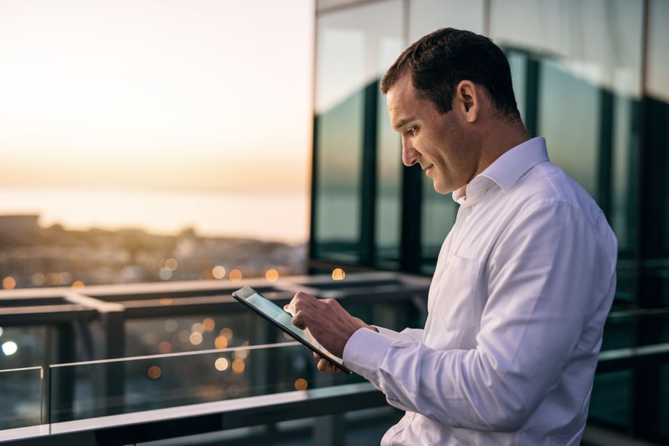 Manager stands on office building balcony, using tablet computer to review success of his procurement inflation strategies.